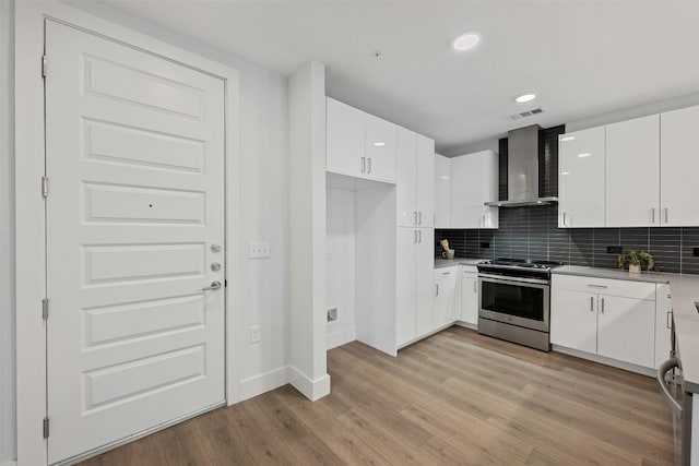 kitchen featuring white cabinetry, wall chimney range hood, stainless steel range oven, light hardwood / wood-style floors, and decorative backsplash