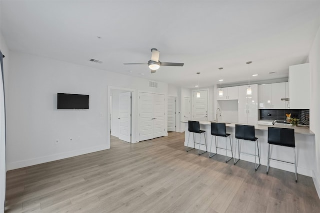 kitchen featuring decorative backsplash, ceiling fan, light hardwood / wood-style flooring, white cabinets, and hanging light fixtures