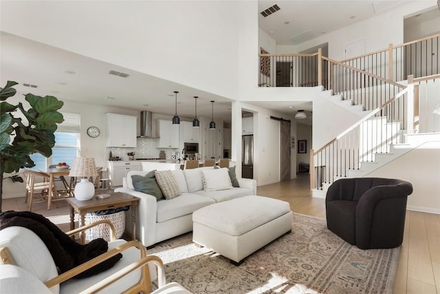 living room with a towering ceiling, a barn door, and light hardwood / wood-style flooring