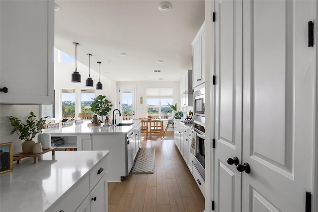 kitchen with sink, light hardwood / wood-style flooring, an island with sink, white cabinets, and decorative light fixtures