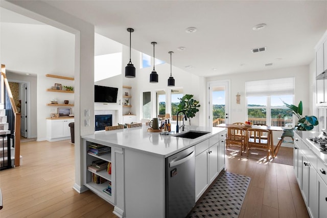 kitchen with pendant lighting, dishwasher, white cabinets, a center island with sink, and light wood-type flooring