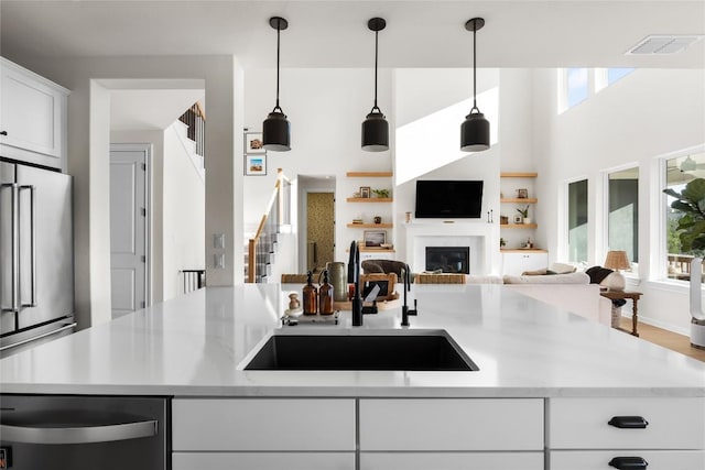 kitchen with appliances with stainless steel finishes, a wealth of natural light, white cabinetry, sink, and hanging light fixtures