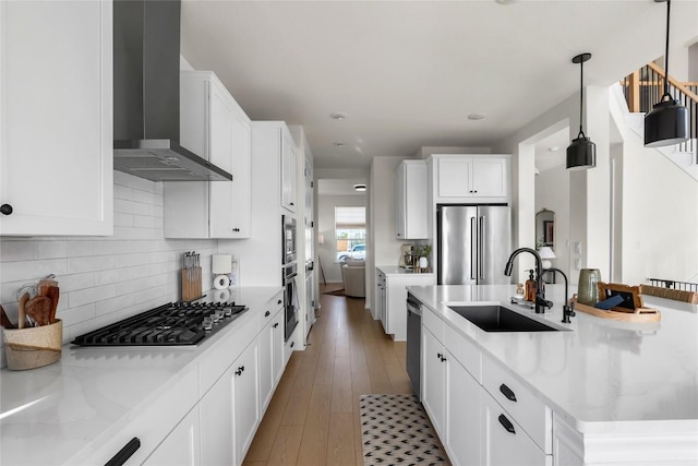 kitchen with appliances with stainless steel finishes, decorative light fixtures, sink, white cabinets, and wall chimney range hood