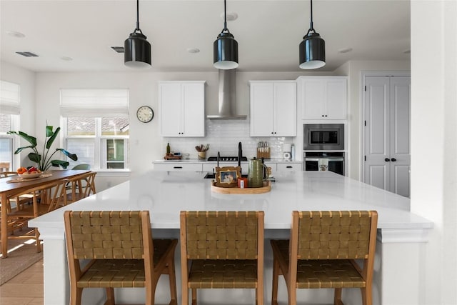 kitchen featuring wall chimney exhaust hood, decorative light fixtures, stainless steel appliances, decorative backsplash, and white cabinets