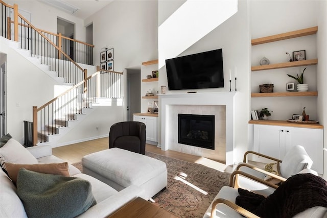 living room featuring built in shelves, light hardwood / wood-style floors, a tile fireplace, and a high ceiling