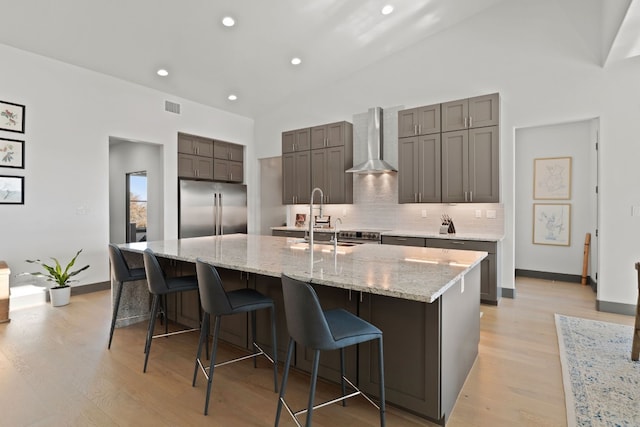 kitchen featuring high end refrigerator, a spacious island, sink, light hardwood / wood-style flooring, and wall chimney exhaust hood