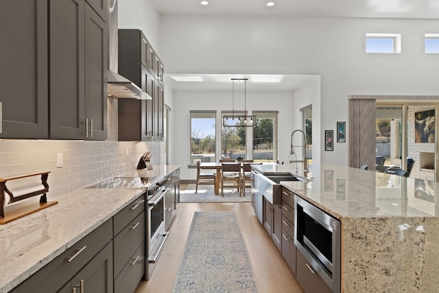 kitchen with sink, stainless steel appliances, light stone counters, pendant lighting, and light wood-type flooring