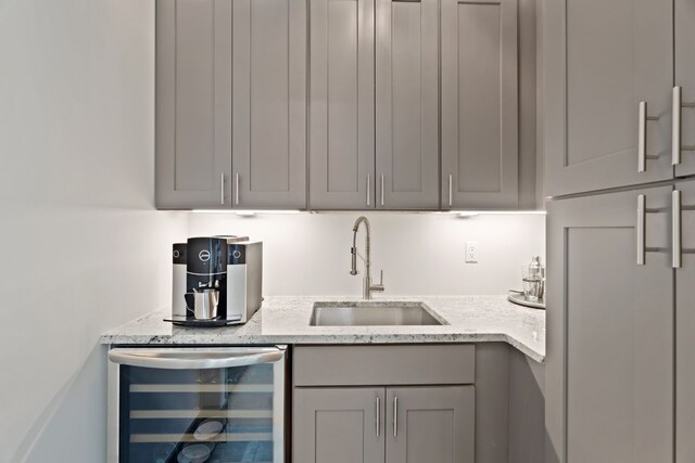 kitchen featuring wine cooler, light stone countertops, sink, and gray cabinets