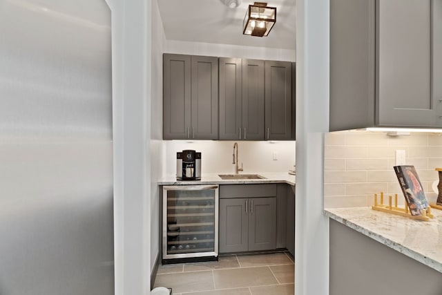 bar featuring light stone counters, wine cooler, gray cabinetry, and sink