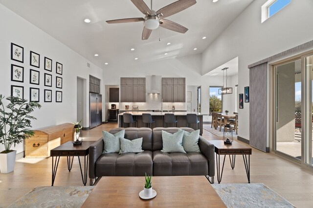 living room featuring ceiling fan with notable chandelier, light hardwood / wood-style flooring, and high vaulted ceiling