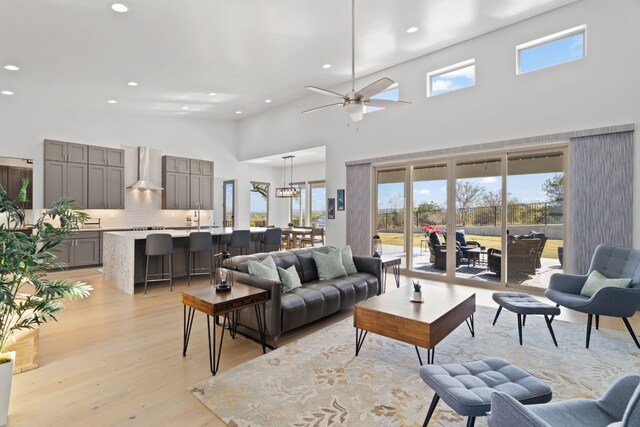 living room with ceiling fan, light hardwood / wood-style floors, and a towering ceiling