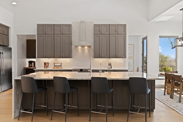 kitchen with stainless steel fridge, light hardwood / wood-style floors, a large island with sink, and wall chimney exhaust hood