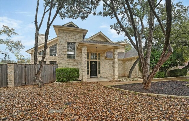 view of front of property featuring stone siding, a chimney, and fence