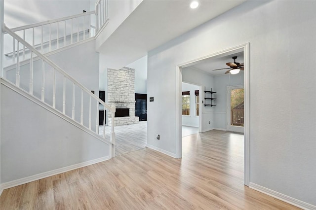 unfurnished living room with ceiling fan, a fireplace, wood finished floors, baseboards, and stairway