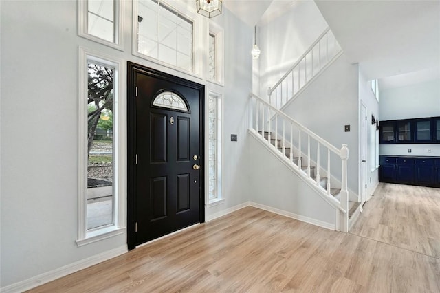 foyer entrance featuring a high ceiling, stairway, light wood-type flooring, and baseboards