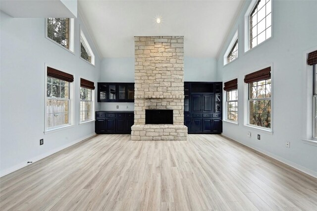 unfurnished living room featuring baseboards, a stone fireplace, a high ceiling, and wood finished floors