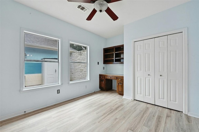 unfurnished bedroom featuring visible vents, a ceiling fan, a closet, built in study area, and light wood finished floors