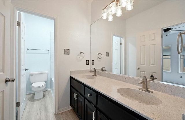 full bathroom featuring wood finished floors, a sink, toilet, and double vanity