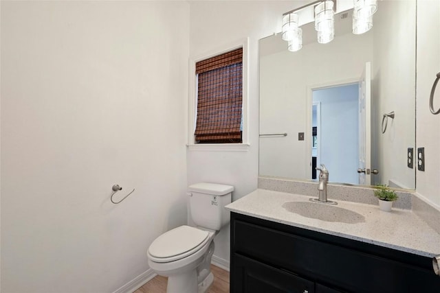 half bathroom featuring baseboards, vanity, toilet, and wood finished floors