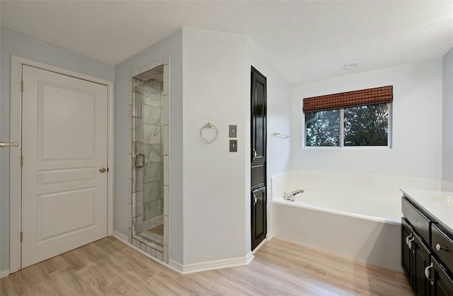 bathroom featuring a garden tub, wood finished floors, vanity, baseboards, and a stall shower