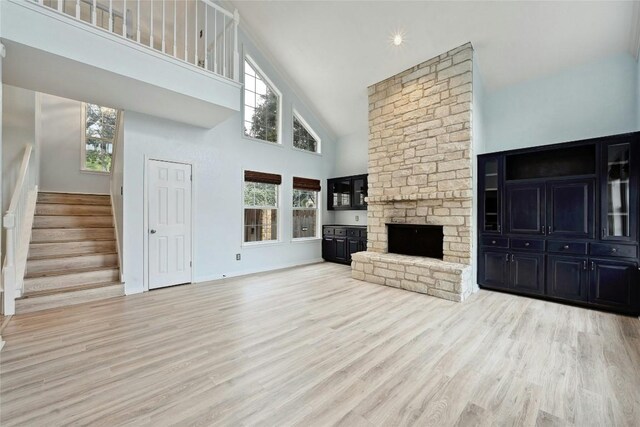 unfurnished living room with high vaulted ceiling, stairway, a fireplace, and wood finished floors