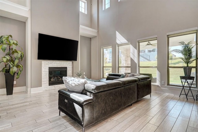 living room with ceiling fan, a stone fireplace, light wood-type flooring, and a towering ceiling