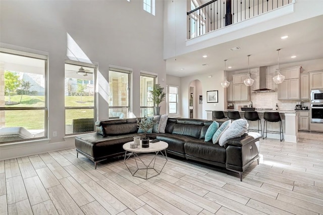 living room featuring a wealth of natural light, ceiling fan, light hardwood / wood-style floors, and a high ceiling