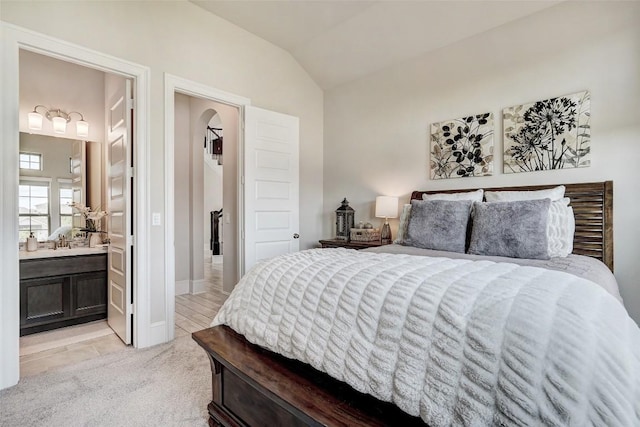 bedroom featuring light carpet, ensuite bathroom, and lofted ceiling