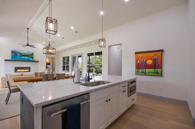 kitchen featuring stainless steel appliances, sink, white cabinetry, hanging light fixtures, and an island with sink