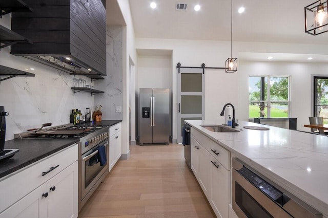 kitchen with dark stone counters, sink, a barn door, appliances with stainless steel finishes, and decorative light fixtures