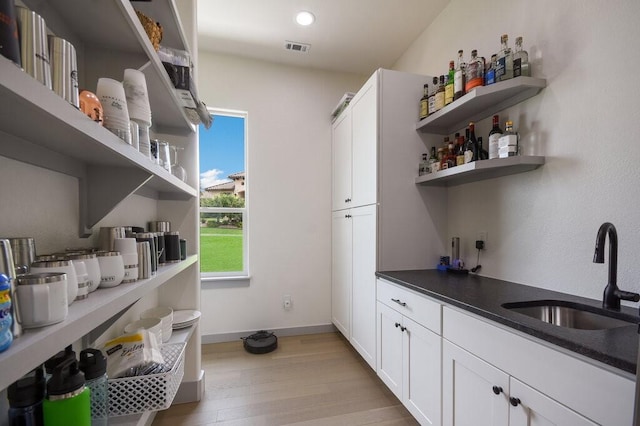 bar with sink, white cabinets, and light hardwood / wood-style floors