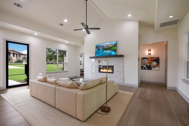 living room featuring a fireplace, light hardwood / wood-style floors, high vaulted ceiling, and ceiling fan