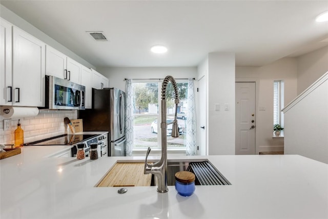 kitchen with stainless steel appliances, white cabinetry, and tasteful backsplash