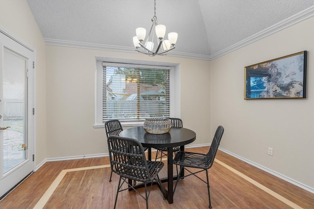 dining area featuring ornamental molding, a textured ceiling, wood-type flooring, a notable chandelier, and lofted ceiling