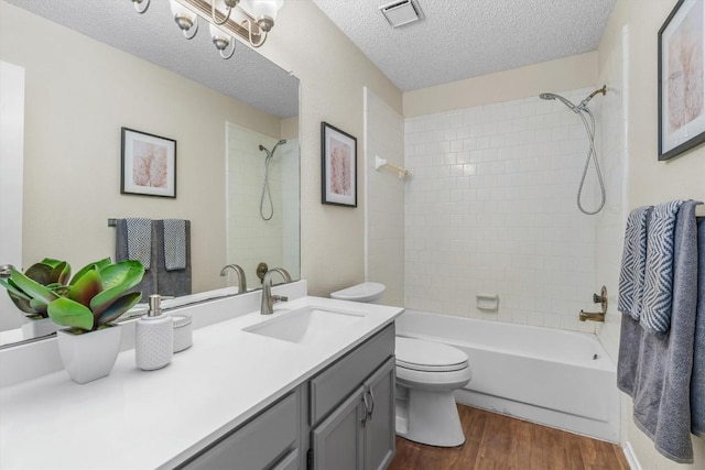 full bathroom featuring hardwood / wood-style floors, vanity, tiled shower / bath combo, toilet, and a textured ceiling