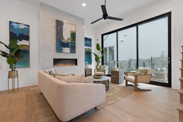 living room with a large fireplace, light hardwood / wood-style flooring, and ceiling fan