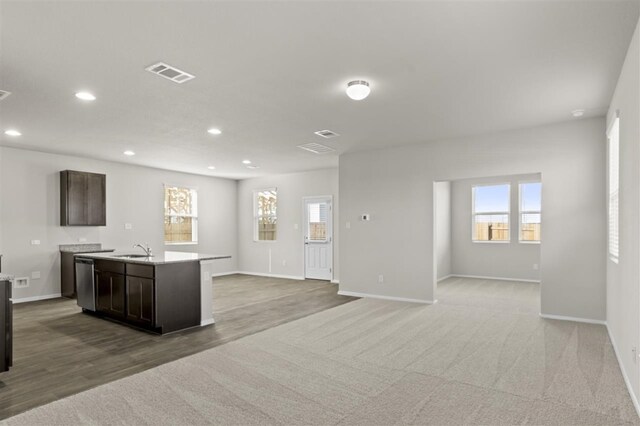 kitchen featuring sink, stainless steel dishwasher, carpet flooring, an island with sink, and dark brown cabinetry