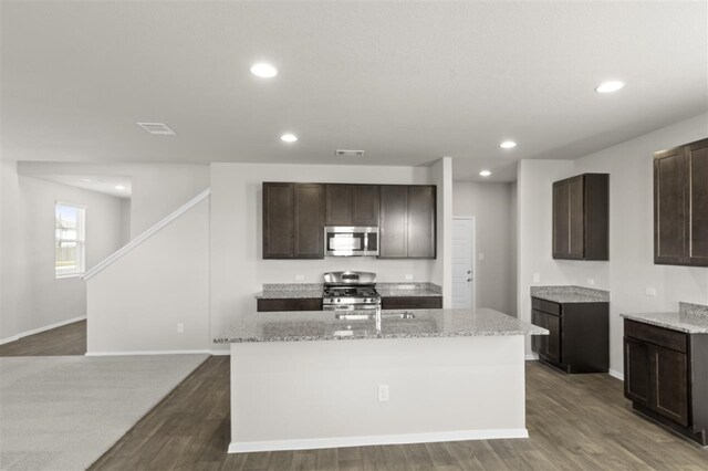 kitchen with a center island with sink, light stone countertops, appliances with stainless steel finishes, dark hardwood / wood-style flooring, and dark brown cabinetry