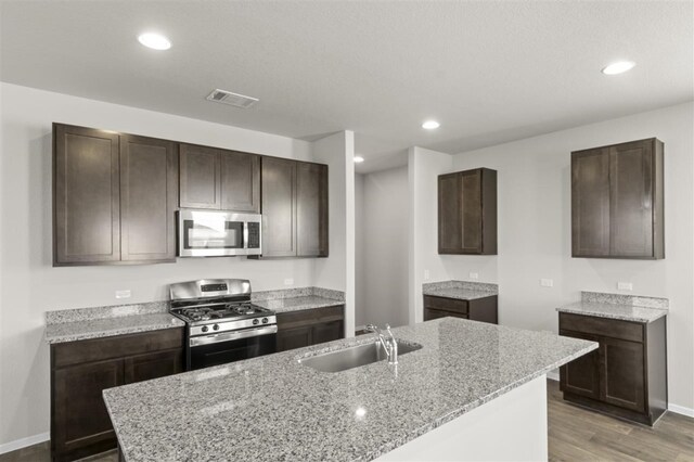 kitchen with light stone countertops, sink, appliances with stainless steel finishes, and an island with sink