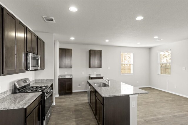 kitchen featuring sink, stainless steel appliances, light stone counters, an island with sink, and dark brown cabinets