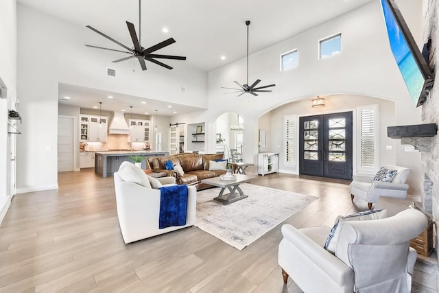 living room with light hardwood / wood-style floors, a healthy amount of sunlight, a stone fireplace, and a towering ceiling