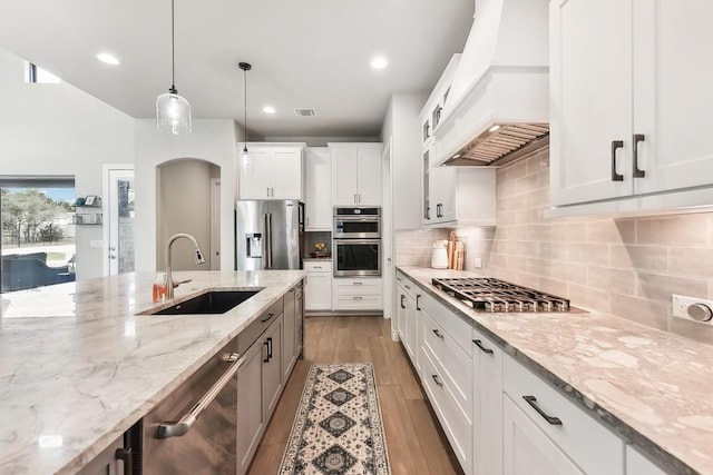 kitchen featuring pendant lighting, white cabinets, appliances with stainless steel finishes, light hardwood / wood-style floors, and custom range hood