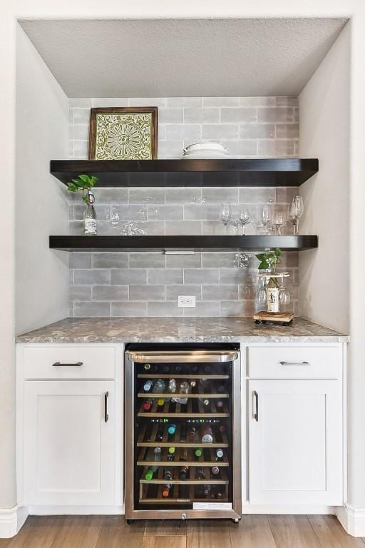 bar featuring light wood-type flooring, white cabinetry, wine cooler, and tasteful backsplash