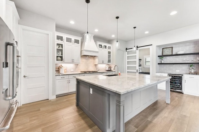 kitchen featuring premium range hood, sink, a barn door, white cabinets, and an island with sink