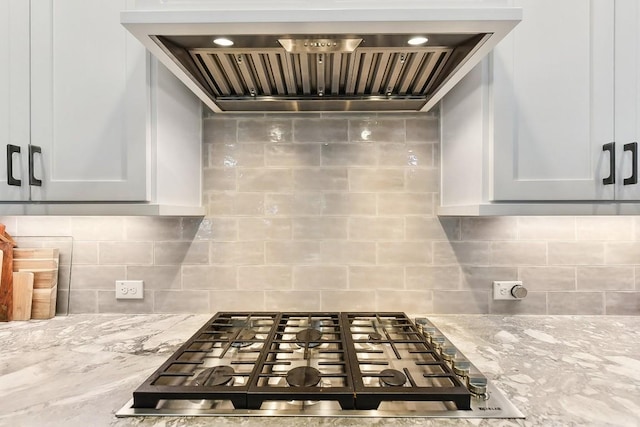 kitchen featuring decorative backsplash, light stone countertops, stainless steel gas cooktop, wall chimney range hood, and white cabinetry