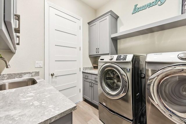 laundry room featuring washer and clothes dryer, cabinets, sink, and light hardwood / wood-style flooring