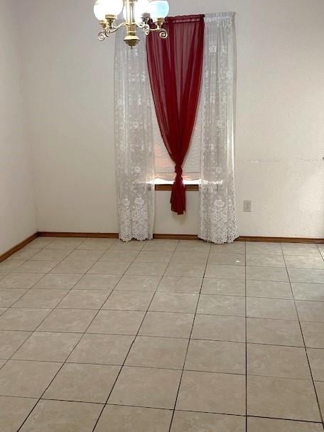 tiled spare room with an inviting chandelier