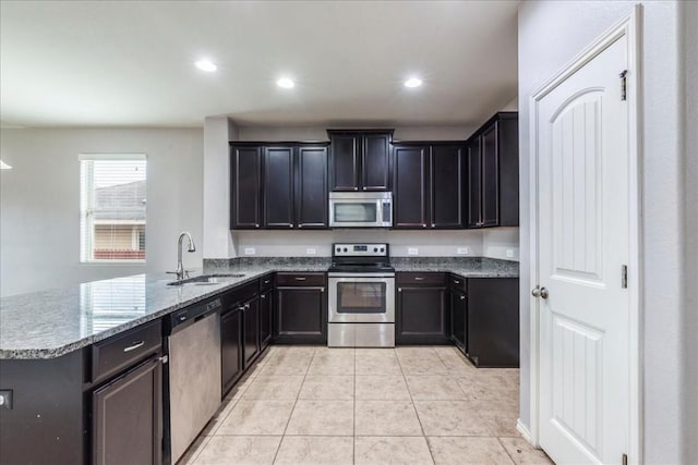 kitchen with light stone countertops, sink, kitchen peninsula, light tile patterned floors, and appliances with stainless steel finishes