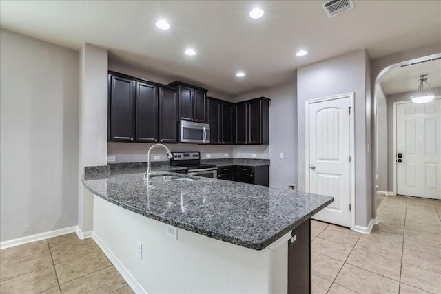 kitchen with sink, dark stone countertops, appliances with stainless steel finishes, light tile patterned flooring, and kitchen peninsula