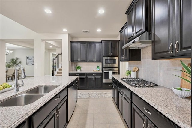 kitchen with appliances with stainless steel finishes, tasteful backsplash, light stone counters, sink, and range hood